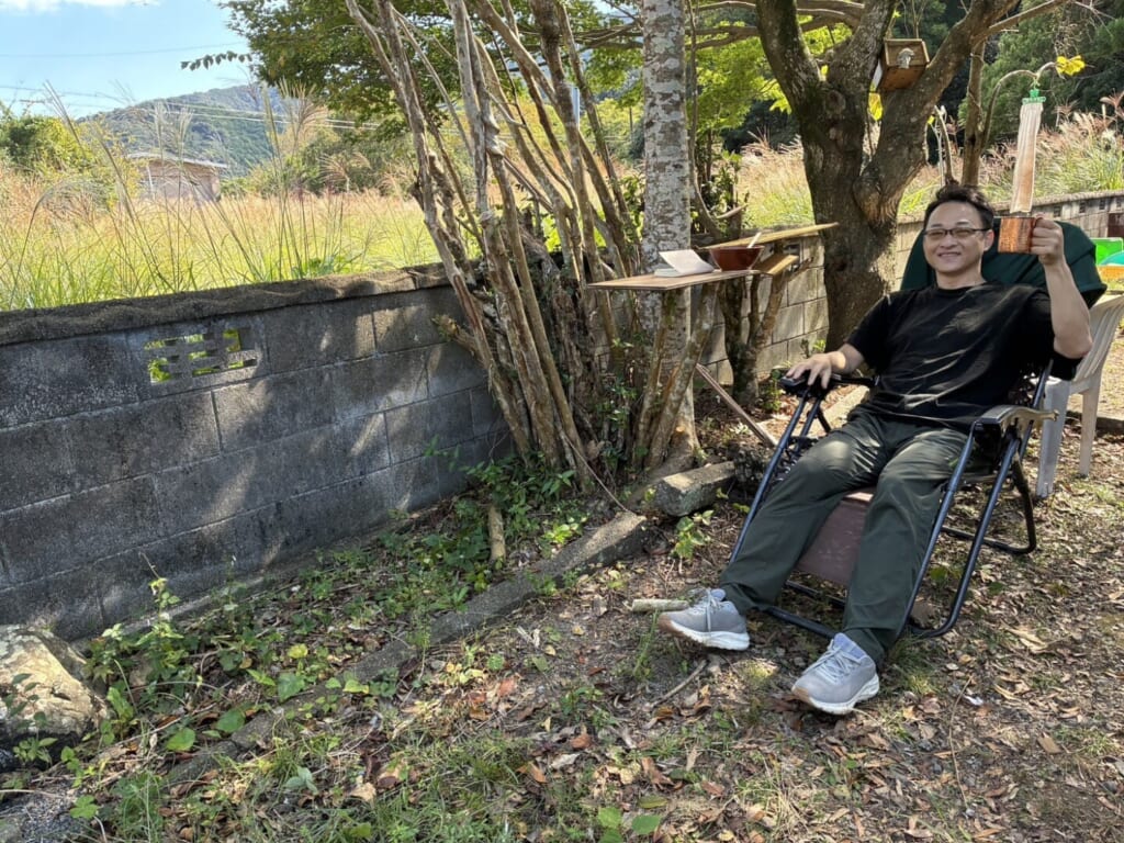田舎の庭でリクライニングチェアに座り、マグカップを手にくつろぐ堀口尚志さん