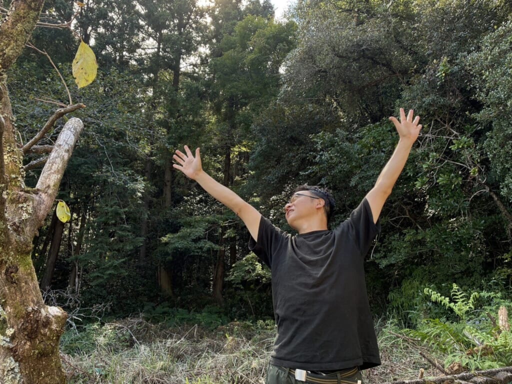 森の中で両手を広げ、空を見上げる堀口尚志さん